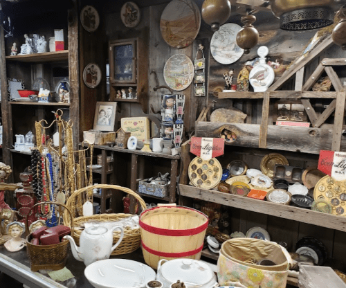 A cozy antique shop display filled with vintage items, including dishes, jewelry, and decorative pieces on wooden shelves.