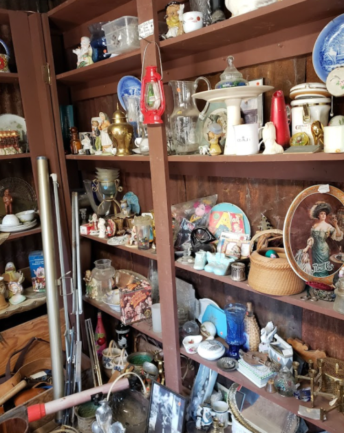 A cluttered shelf filled with various antiques, collectibles, and decorative items in a rustic setting.