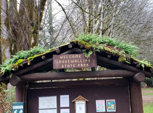 Welcome sign at Dosewallips State Park, surrounded by trees and moss-covered roof.