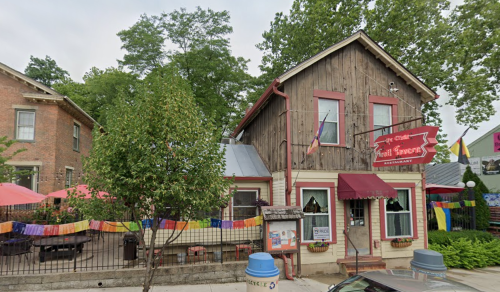 A rustic building with a sign reading "Fruit Tavern," surrounded by trees and colorful outdoor seating.