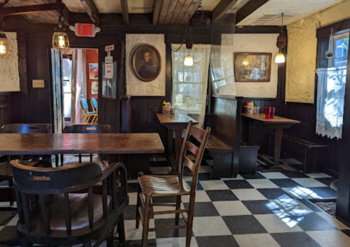 Cozy interior of a rustic restaurant with wooden tables, chairs, and checkered flooring, featuring vintage decor.