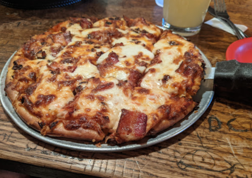 A freshly baked pizza with melted cheese and toppings, served on a metal tray on a wooden table.