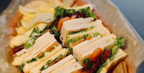 A close-up of a sandwich with layers of turkey, lettuce, and tomato, served with potato chips on the side.