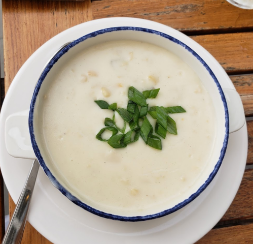 A bowl of creamy soup topped with fresh green herbs, placed on a wooden table.