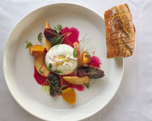 A plate with burrata cheese, colorful roasted beets, and a slice of toasted bread on the side.