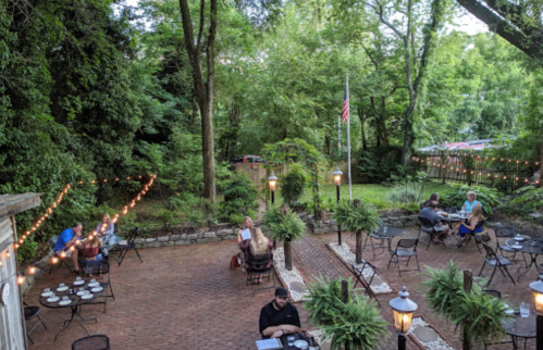 Outdoor dining area with string lights, tables, and greenery, featuring patrons enjoying their meals in a serene setting.