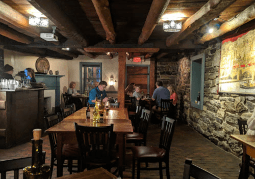 Cozy restaurant interior with wooden beams, stone walls, and diners at tables enjoying their meals.