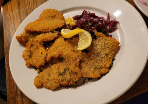 A plate of golden-brown fried fish fillets garnished with lemon slices and served with red cabbage and a side of coleslaw.