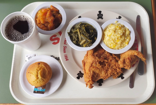 A tray with fried chicken, collard greens, macaroni and cheese, sweet potatoes, cornbread, and a cup of coffee.