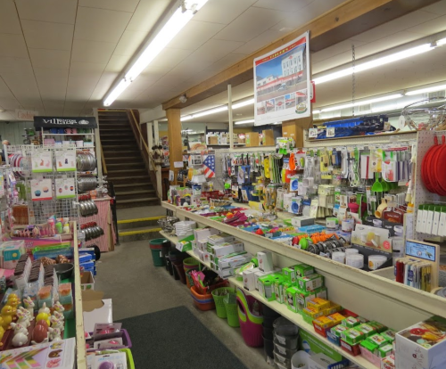 A well-stocked store aisle filled with various kitchen tools, gardening supplies, and household items. Stairs in the background.