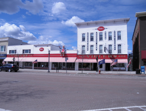 A large white building with red awnings and a sign reading "Vidler's" under a blue sky with fluffy clouds.