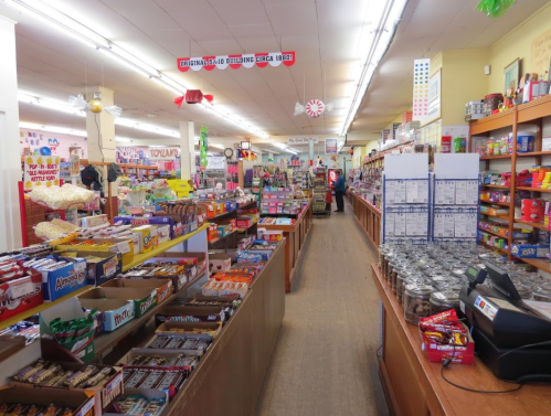 A colorful candy store aisle filled with various snacks, candies, and treats on wooden shelves.