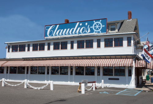 A waterfront restaurant named Claudio's with a large sign and striped awnings, featuring a nautical theme.