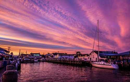 A serene harbor at sunset, featuring colorful clouds, boats, and charming waterfront buildings.