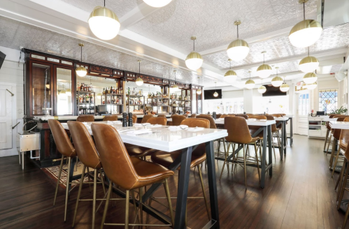A modern restaurant interior featuring a bar, high-backed chairs, and stylish pendant lighting.