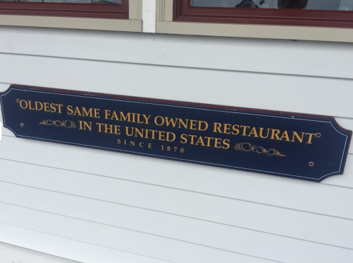 Sign reading "Oldest Same Family Owned Restaurant in the United States Since 1870" on a white building.