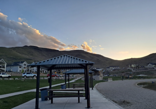 A scenic view of a park with picnic shelters, mountains, and a sunset sky in the background.