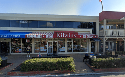 A storefront with a red and white awning reading "Kilwins" offering chocolates, fudge, and ice cream.