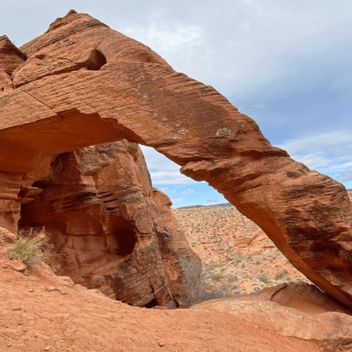 A natural rock arch in a desert landscape, surrounded by red sandstone formations and a blue sky.