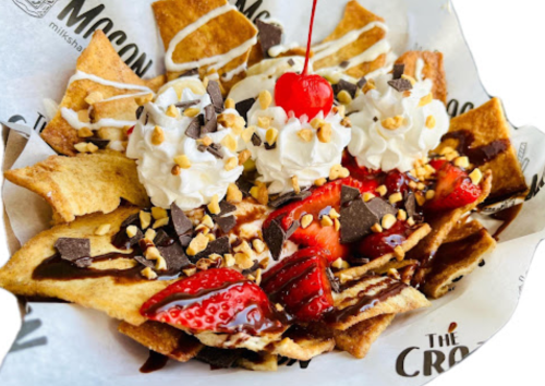 A dessert bowl with crispy tortilla chips topped with strawberries, whipped cream, chocolate, nuts, and a cherry.