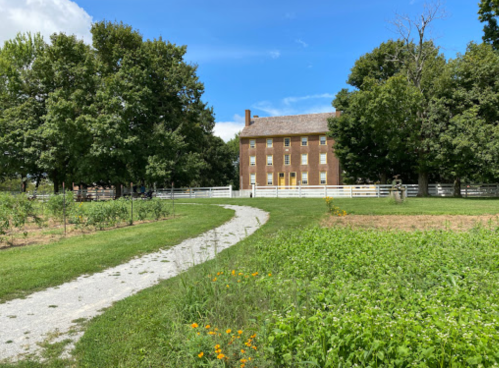 A historic brick house surrounded by trees and a grassy path, with a clear blue sky in the background.