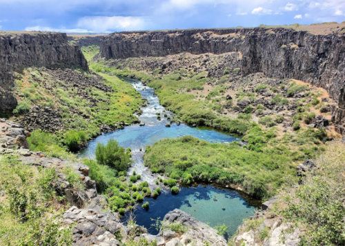 A scenic view of a river winding through a lush green canyon surrounded by rocky cliffs under a blue sky.