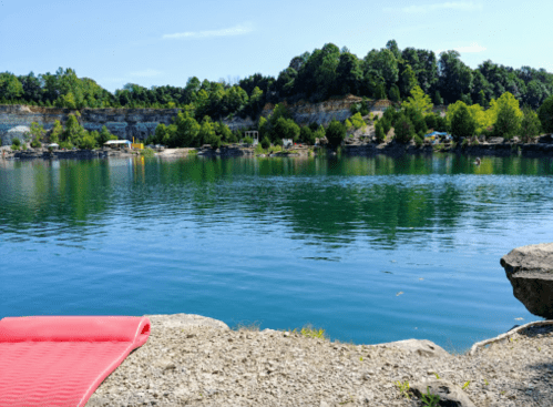 A serene lake surrounded by greenery and rocky cliffs, with a red float nearby on the shore.