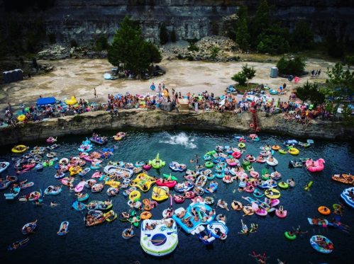 Aerial view of a crowded swimming area with colorful floats and people enjoying a sunny day by the water.