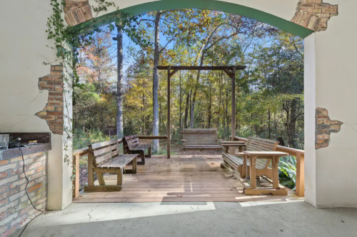 A rustic outdoor seating area with wooden benches and swings, surrounded by trees and autumn foliage.