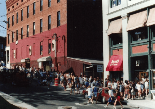 A busy street scene with a large crowd of people, shops, and buildings in a vibrant urban setting.