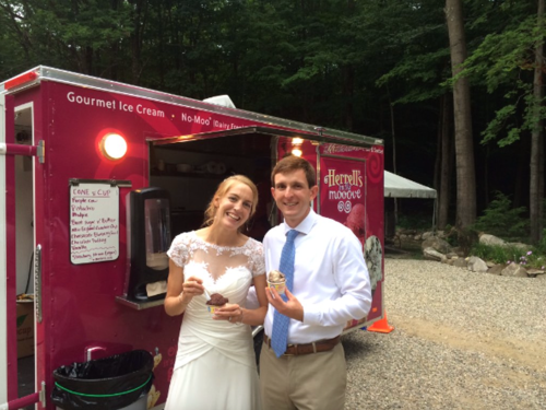 A bride and groom enjoy ice cream from a pink food truck in a wooded outdoor setting.