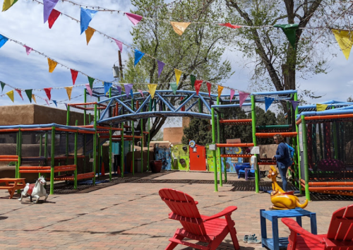 Colorful outdoor play area with trampolines, festive banners, and red chairs under a blue sky.
