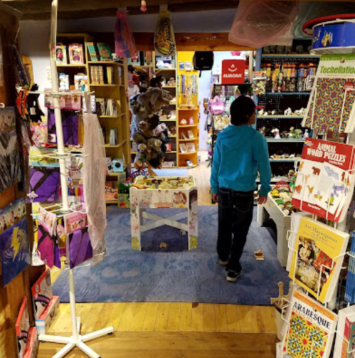 A child walks through a colorful store filled with toys, puzzles, and various merchandise on display.