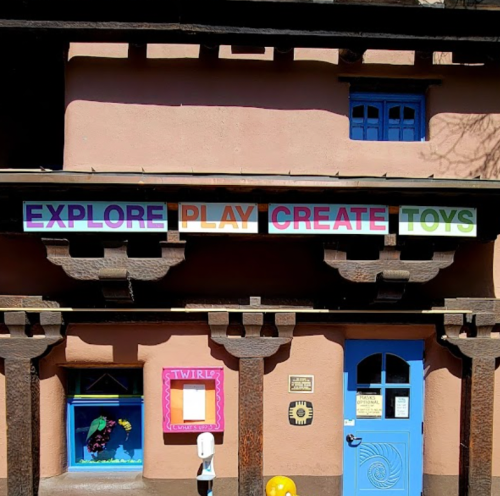 Colorful sign on a building reads "EXPLORE PLAY CREATE TOYS," with a playful design and bright blue windows.