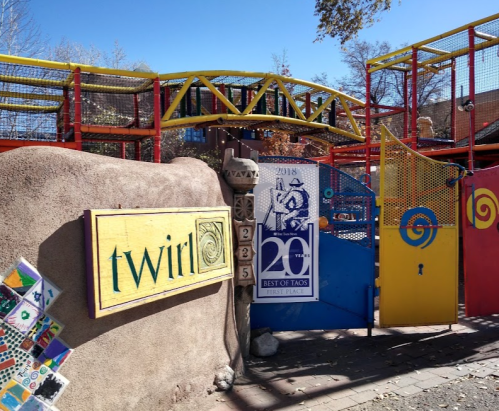 Colorful entrance to a playground with a sign reading "twirl" and various artistic designs on the walls.