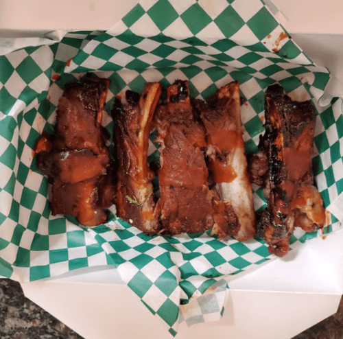 A box containing several pieces of ribs drizzled with barbecue sauce on green and white checkered paper.