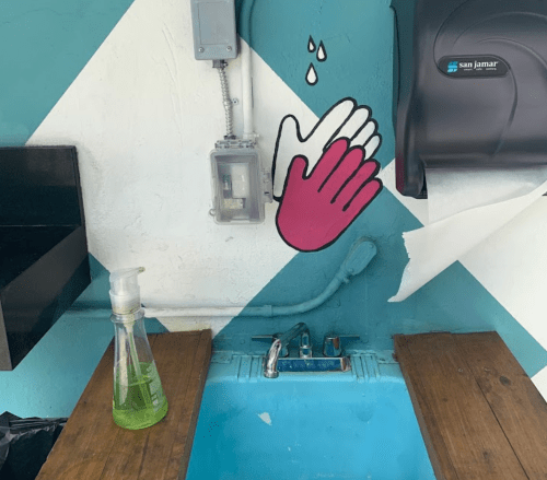 A sink with a soap dispenser and a handwashing mural on the wall, featuring a pink hand and water droplets.