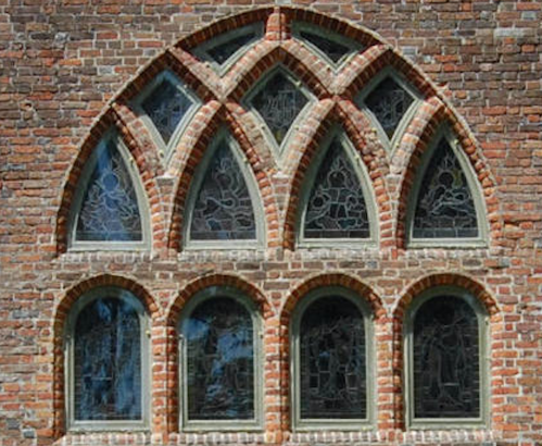 Gothic-style brick wall with arched stained glass windows featuring intricate designs.