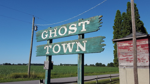 Signpost reading "GHOST TOWN" with a clear blue sky and fields in the background.