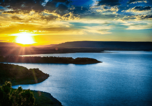 Sunset over a tranquil lake, with vibrant colors reflecting on the water and mountains in the background.