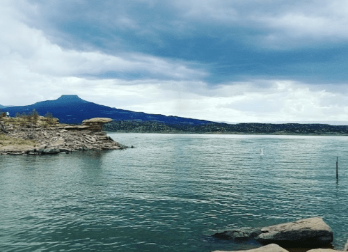 A serene lake scene with rocky shores, mountains in the background, and a cloudy sky above.