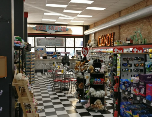 A colorful store interior featuring a soda fountain, candy display, and shelves of toys and sunglasses.