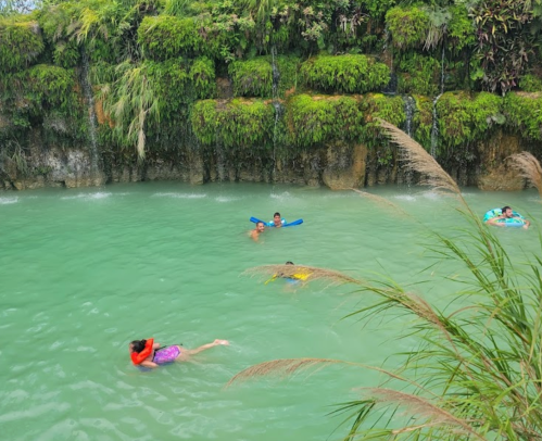 Children swimming in a turquoise pool surrounded by lush greenery and rocky cliffs.