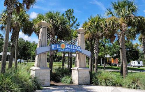 A welcoming sign for Florida surrounded by palm trees and blue skies.