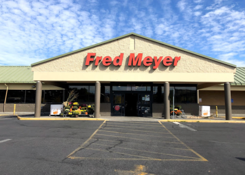 Exterior of a Fred Meyer store with a blue sky and clouds in the background, featuring a parking lot in front.
