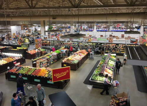 Aerial view of a grocery store with colorful produce displays and shoppers browsing the aisles.