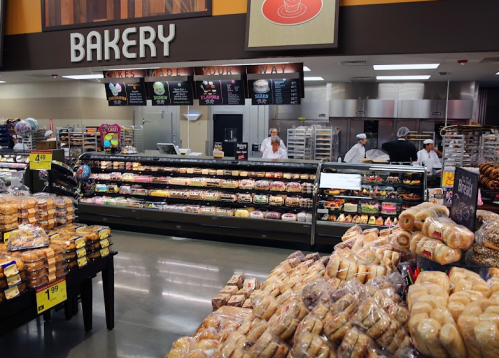 A bakery section in a store with various baked goods and staff behind the counter. Fresh bread and pastries are displayed.