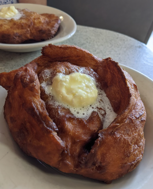 A golden-brown fried pastry topped with a dollop of creamy butter on a white plate.