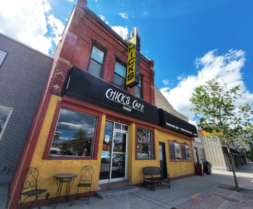 A colorful café building with a sign reading "Chick's Café," featuring outdoor seating and a bright blue sky.