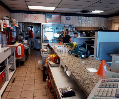 A cozy diner interior with a long counter, kitchen area, and decor including an American flag and a small toy truck.